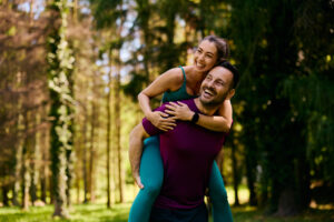 Happy couple enjoying outdoor activity in a forest, emphasizing wellness and active lifestyle, relevant to Galen Healthcare & Aesthetics' focus on health and beauty treatments.